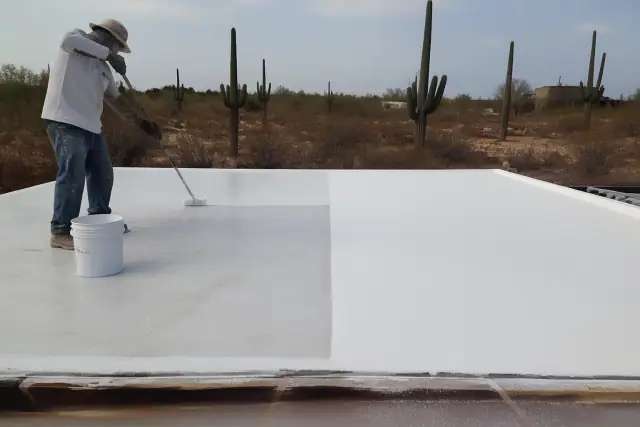 Crew member pressure washing a roof in Tucson, AZ to show the difference between one and two coats of reflective coating.