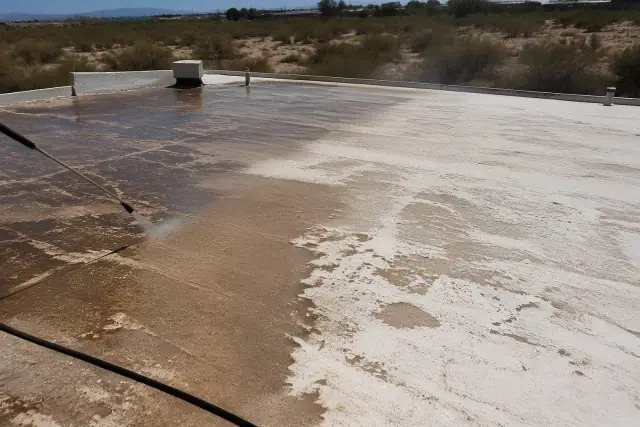 A worker pressure washing a weathered roof surface before applying reflective coating in Flowing Wells, AZ.