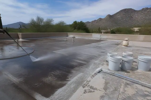 Pressure washer cleaning a weathered roof before coating in Oro Valley, AZ, with buckets and rollers nearby.