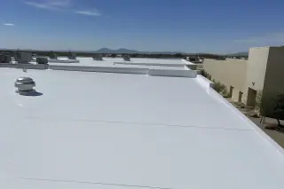 Smooth reflective roof coating on a flat commercial building with rocky desert landscape in Tucson, AZ.