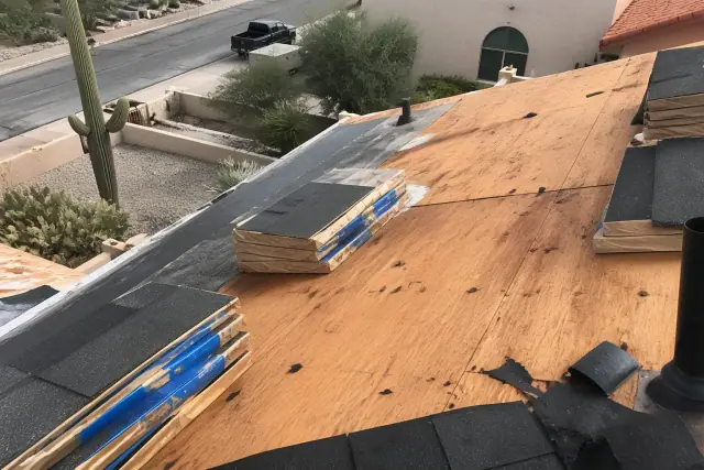 Technician kneeling on a steep roof in Tucson, AZ, securing shingles to wooden decking during a home repair.
