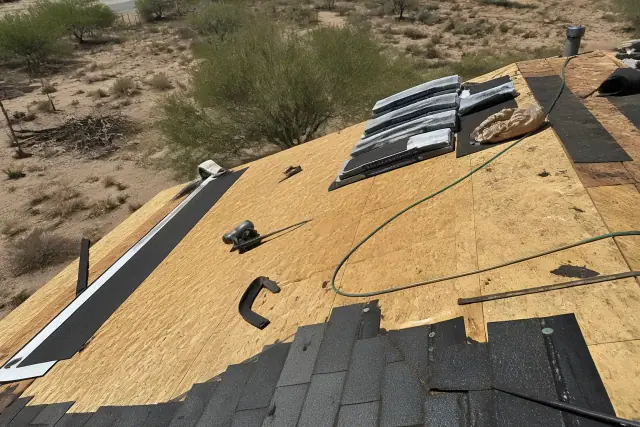 Technician kneeling on a steep shingled roof while installing materials on a sunny day in Flowing Wells, AZ.
