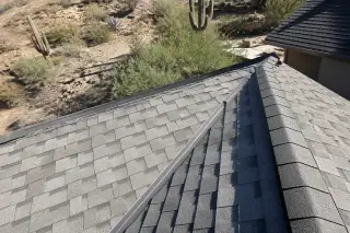 New asphalt shingles and ridge caps on a roof repair project in Tucson, AZ with saguaro cacti in the background.