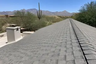 A finished roof repair with new shingles and ridge capping on a home in Tucson, AZ with a saguaro cactus in the background.