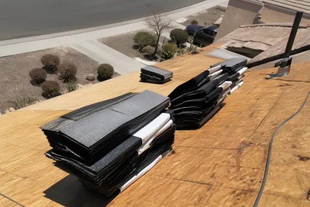 A technician kneeling on a steep-sloped roof securing shingles to the decking in Tucson, AZ.