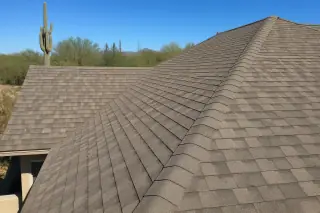 Newly installed asphalt shingles and ridge lines on a home roof under the desert sun in Tucson, AZ with a Saguaro cactus.