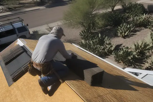 Contractor installing asphalt shingles on a steep residential roof in Tucson, AZ, with prickly pear cacti in the yard.