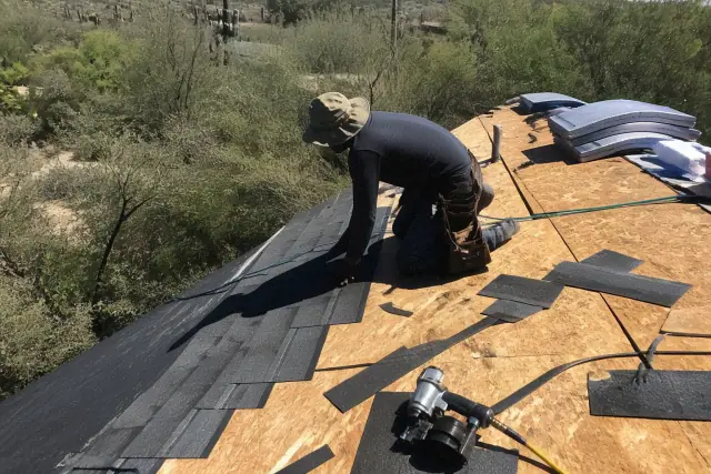 Technician installing shingle roofing on a steep pitched roof in Tucson, AZ with desert landscape in the background.