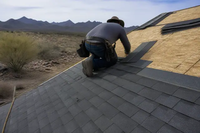 A technician installing shingles on a steep roof in Vail, AZ with desert landscape in the background.