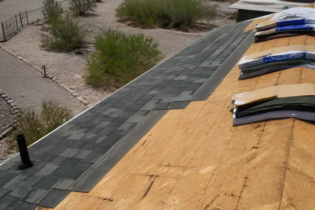 New asphalt shingles being installed on a roof in Flowing Wells, AZ, with bundles on wooden decking and desert landscape.
