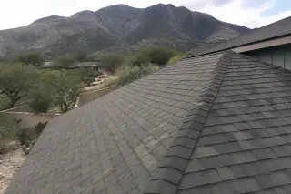 Completed shingle roof with uniform alignment and ridge caps set against desert mountains in Tucson, AZ.