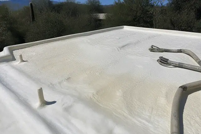 Polyurethane foam being sprayed onto a flat roof in Tucson, AZ with desert vegetation in the background.