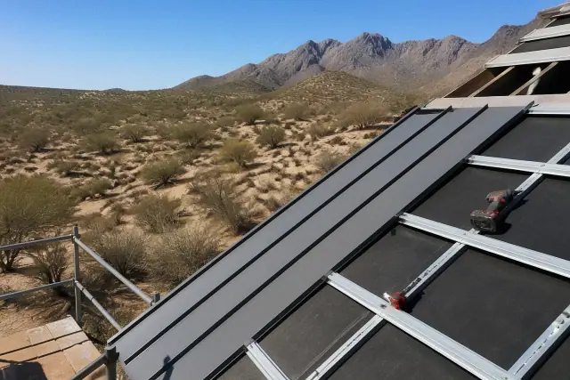Vertical standing seam metal panels being installed on a sloped roof in Tucson, AZ with desert mountains in the background.