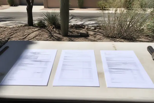 Three roofing estimates laid out on a workbench at a jobsite in Tucson, AZ, with desert scenery in the background.