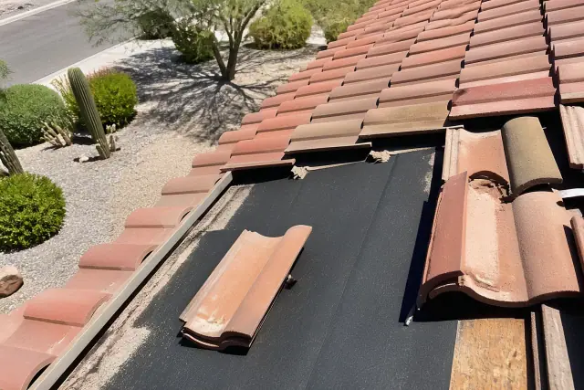 Roofer inspecting clay roof tiles and underlayment on a house in Sahuarita, AZ.