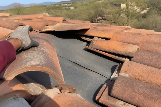 Roofer inspecting waterproof underlayment and clay tiles during a roof repair in Vail, AZ.