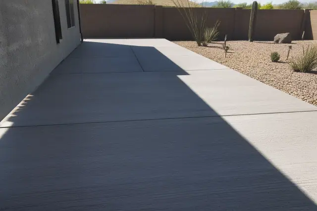 Broom-finish concrete patio slabs with desert gravel landscaping under bright sunlight in Tucson, AZ.