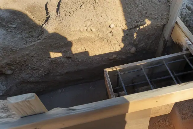 Wooden foundation forms set in a trench with exposed caliche and clay soil layers at a job site in Tucson, AZ.