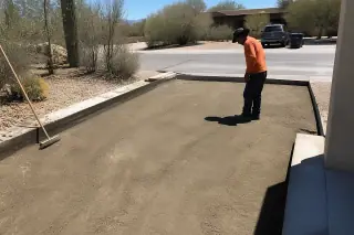 Worker inspecting a cleared driveway site with a broom in a Tucson, AZ desert landscape.
