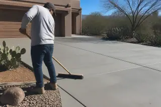 Contractor sweeping a finished concrete driveway near prickly pear cactus in Tucson, AZ.