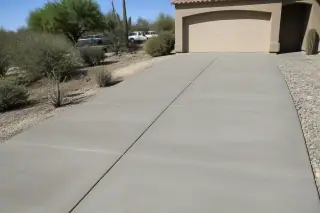 Freshly poured gray concrete driveway with wooden formwork and Sonoran desert vegetation in Tucson, AZ.