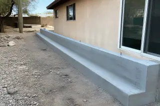 Cured concrete foundation wall with anchor bolts in a gravel-covered Tucson, AZ residential yard.