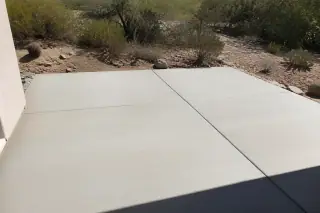Smooth light-gray concrete patio slab surrounded by Sonoran desert scrub in Tucson, AZ under harsh midday sun.