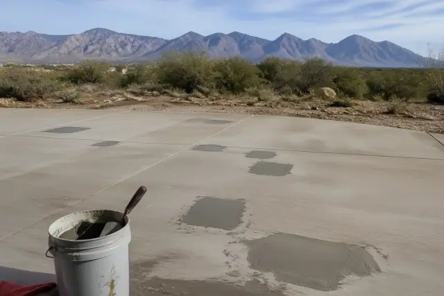 A contractor troweling bonding compound to repair damaged concrete flooring in Oro Valley, AZ with mountain views.