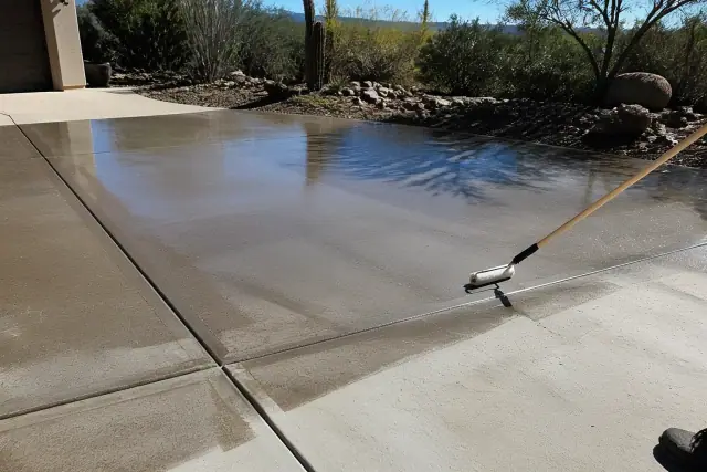 A contractor applying clear concrete sealer with a roller brush to a residential driveway in Green Valley, AZ.