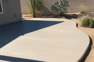 Finished gray concrete patio slab next to prickly pear cacti in a sunny Tucson, AZ residential yard.