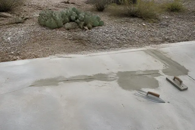 Worker troweling bonding compound into a concrete driveway crack in Tucson, AZ with desert landscaping in the background.