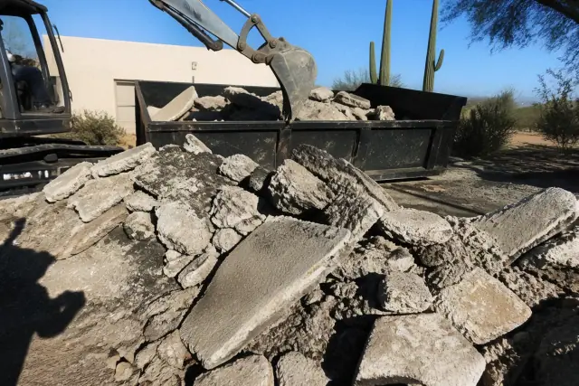 Heavy machinery breaking apart an old concrete driveway into rubble at a job site in Tucson, AZ.