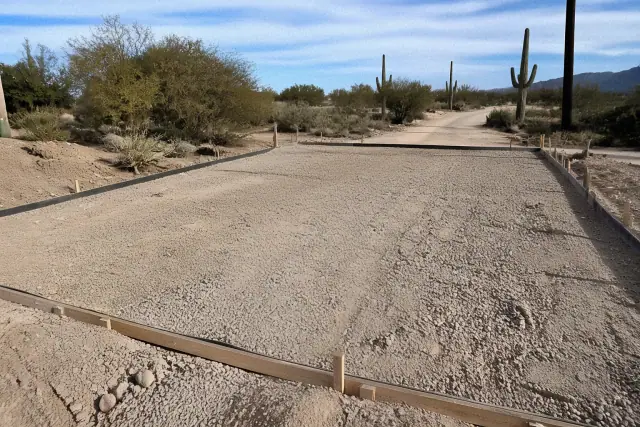 Gravel base prepared for a new concrete driveway installation in Tucson, AZ with desert terrain in the background.