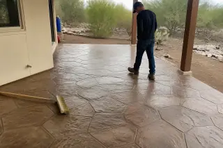 Worker inspecting a finished stamped concrete patio with desert landscaping in Tucson, AZ.