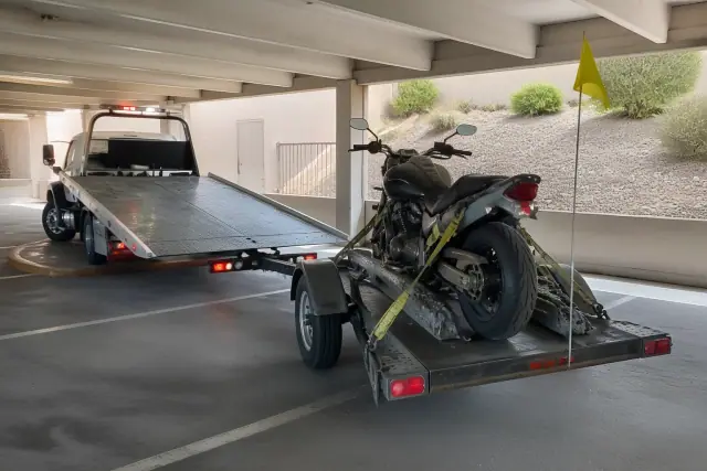 Tow truck maneuvering in a Tucson, AZ parking garage to pick up a motorcycle secured on a trailer.