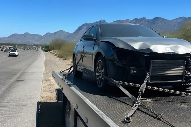 A damaged car being secured with heavy-duty chains on a flatbed truck in Casas Adobes, AZ near the Santa Catalina Mountains.
