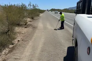 Technician sweeping debris from a desert highway shoulder after a roadside cleanup in Tucson, AZ.