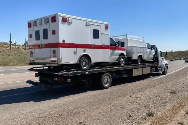 Ambulance and service vehicle secured on a flatbed tow truck on a highway in Tucson, AZ.