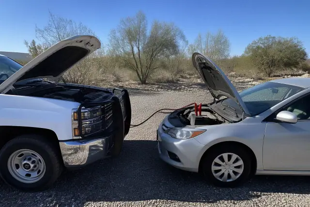 Service vehicle jump-starting a sedan with jumper cables on a gravel lot in Tucson, AZ.