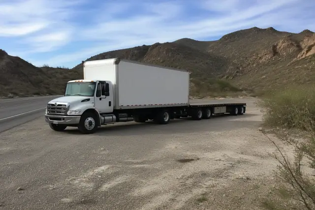 A heavy-duty truck towing a large transport trailer parked in a desert pull-off area in Tucson, AZ.