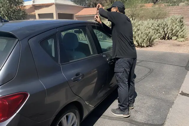 Technician using a lockout tool to open a car door in a residential driveway in Tucson, AZ.