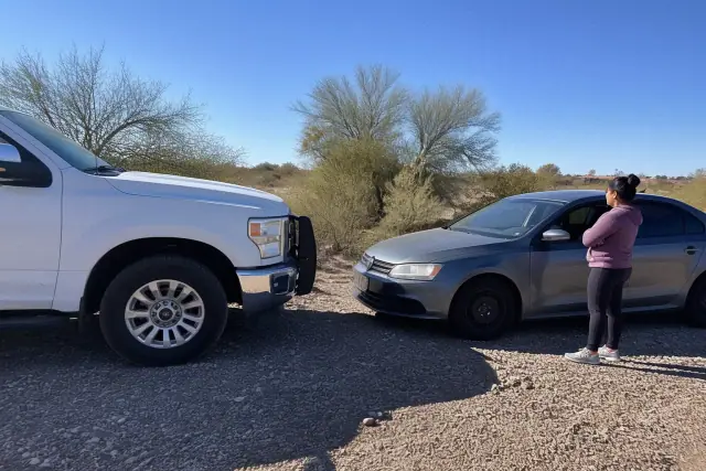 A jump-start service vehicle parked nose-to-nose with a sedan on a rocky lot in Marana, AZ, with the owner standing nearby.