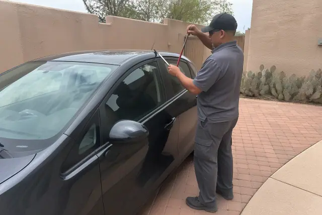Technician using a lockout tool on a car door in a suburban driveway in Tucson, AZ.