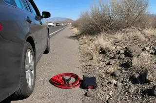 Coiled jumper cables and a portable battery pack on volcanic soil by a highway in Tucson, AZ.
