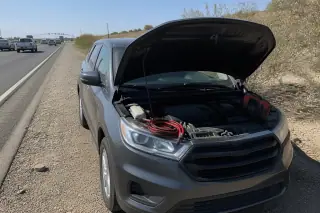 Coiled jumper cables and diagnostic equipment near a car on a gravel highway shoulder in Tucson, AZ.