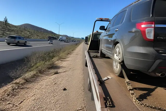 A vehicle being secured onto a flatbed tow truck on a desert highway shoulder in Tucson, AZ.