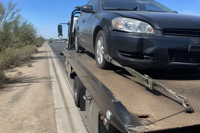 Flatbed tow truck recovering a disabled sedan on a roadside in Tucson, AZ, showing securement hardware and winch lines.