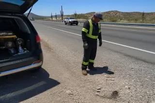 Technician inspecting a highway shoulder for debris after a tow in Tucson, AZ, with saguaro cacti in the background.