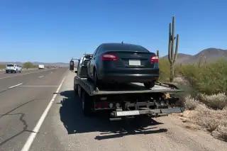 Vehicle securely loaded on a flatbed tow truck parked on a gravel shoulder in Tucson, AZ, with desert landscape background.