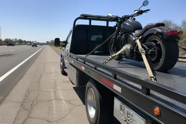 Flatbed truck securing a motorcycle on a highway shoulder in Tucson, AZ.